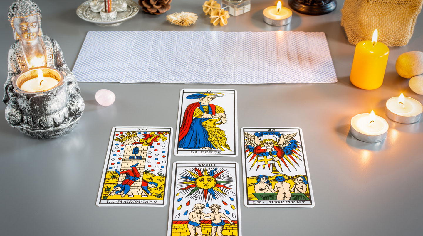 Gros plan sur des mains tenant délicatement une carte de tarot sur une surface en bois clair, avec une tasse de thé et une bougie en arrière-plan flou, dans une atmosphère contemplative et apaisante